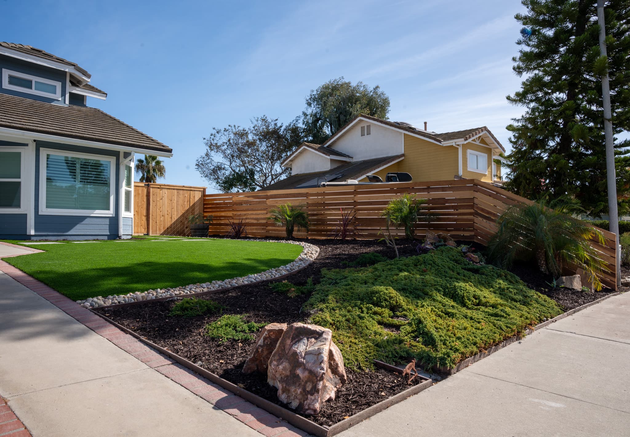 Modern front yard with artificial turf, custom wooden fence, and landscaped garden.