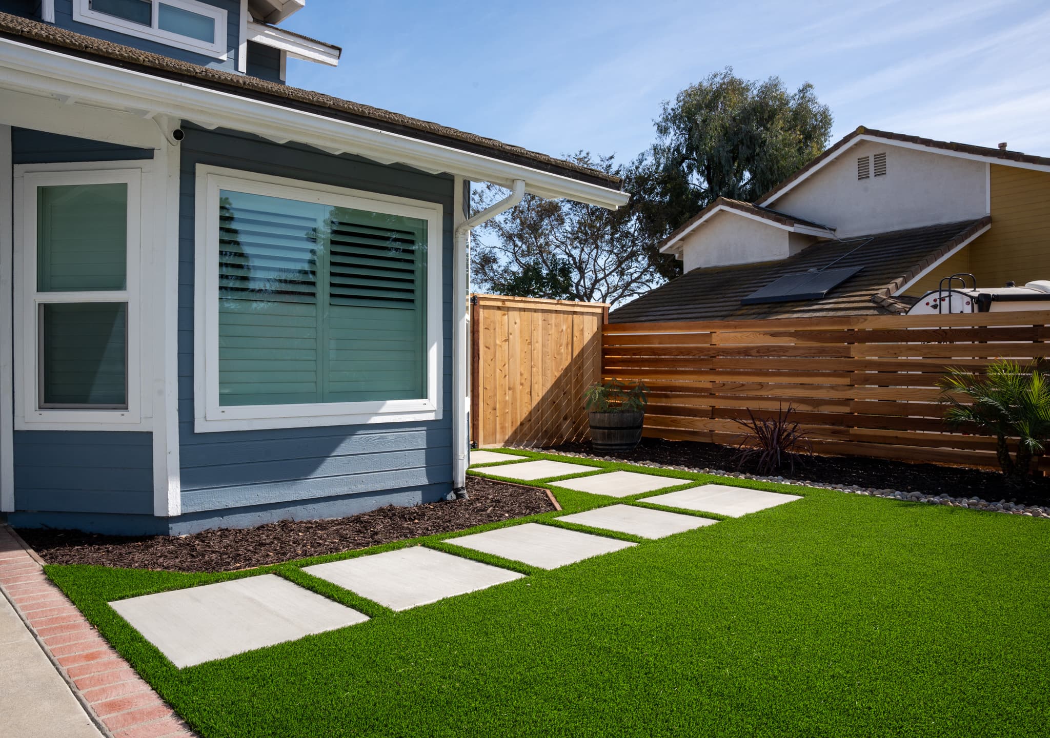 Close-up of artificial grass bordered by smooth river stones and concrete stepping stones.