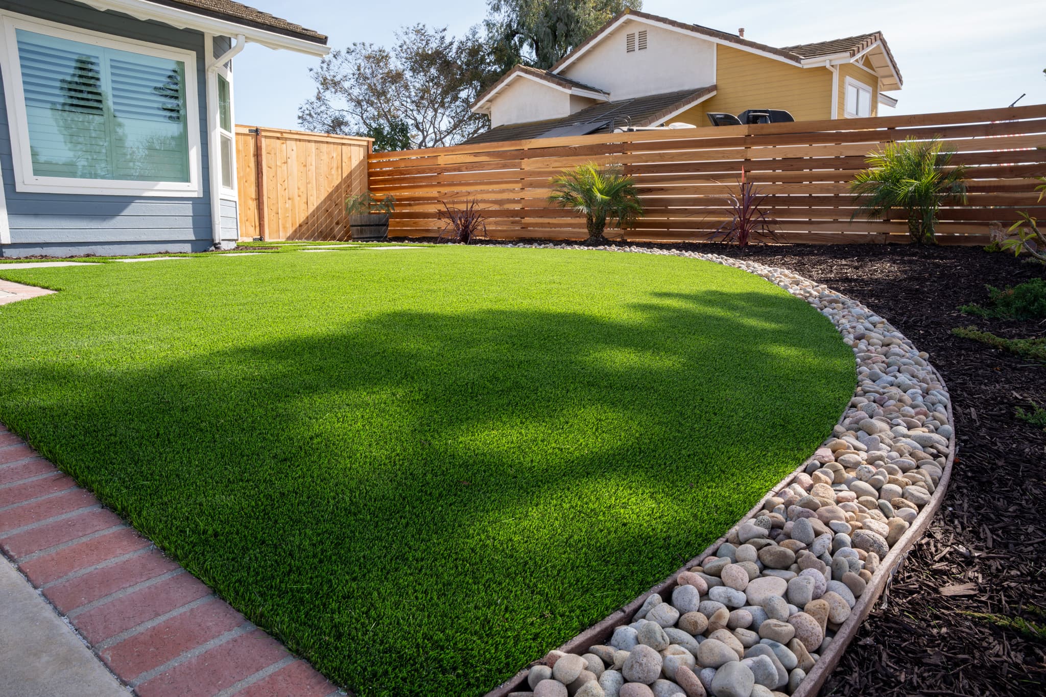 Well-manicured artificial lawn with mulch, rocks, and modern wooden fencing.