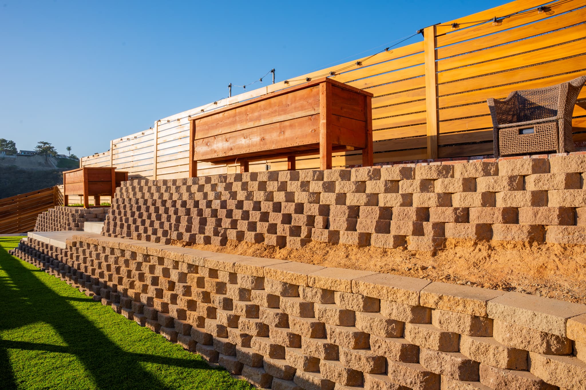 A terraced backyard featuring brick and concrete retaining walls, raised garden planters, and a modern wooden fence.