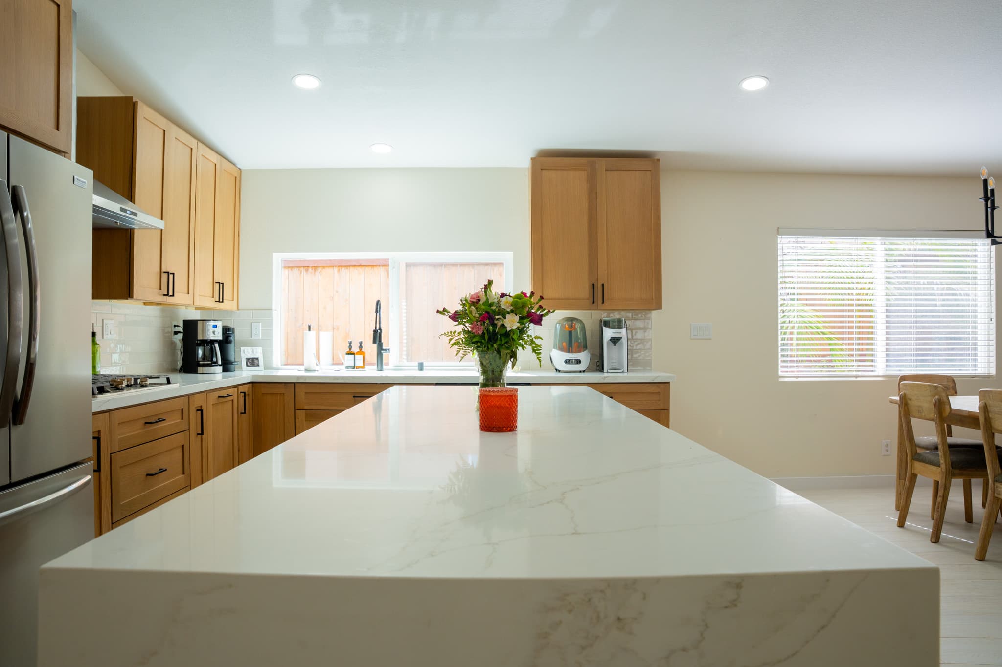 Open-concept kitchen with a white quartz waterfall island and wooden cabinets.